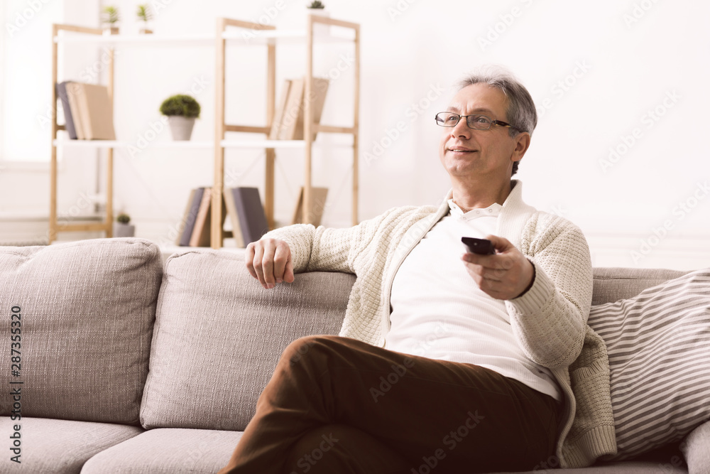 Retired man watching tv with remote control