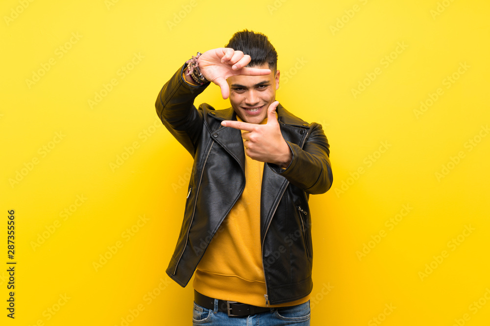 Young man over isolated yellow background focusing face. Framing symbol
