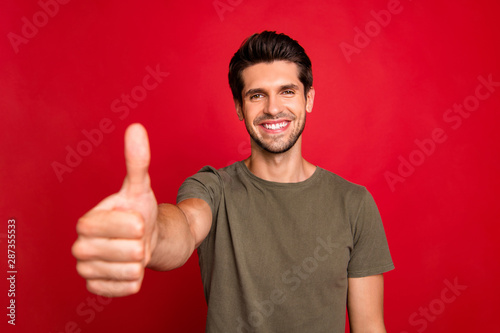 Closeup photo of amazing guy holding arm showing like symbol wear grey t-shirt isolated on red background