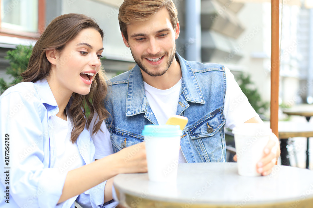 Attractive young couple in love drinking coffee while sitting at the cafe table outdoors, using mobile phone. Attractive young couple in love drinking coffee while sitting at the cafe table outdoors, using mobile phone.