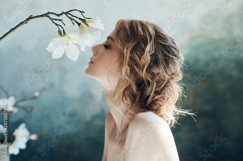 Perfect bride, portrait of a girl in a long white dress. Beautiful hair and clean delicate skin. Wedding hairstyle blonde woman. Girl with a white flower in her hands
