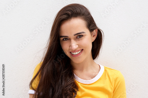 front portrait of young brunette woman smiling against white wall