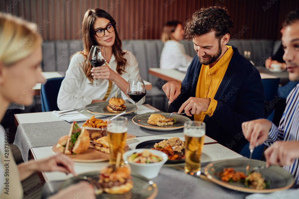Multiethnic friends sitting at restaurant, drinking alcohol, chatting and having burgers for dinner. Multiethnic friends sitting at restaurant, drinking alcohol, chatting and having burgers for dinner.