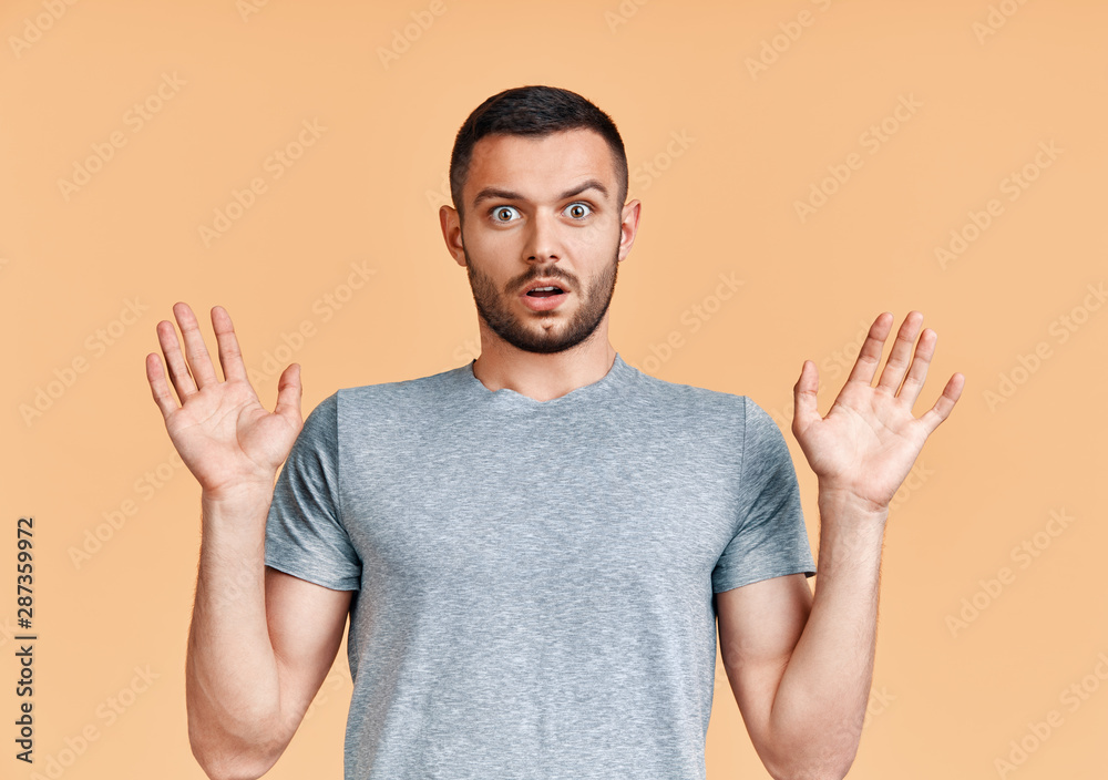 Shocked young man with arms up looking amazed in camera over yellow background