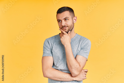 Young thoughtful man thinking and looking aside on copy space isolated on yellow background