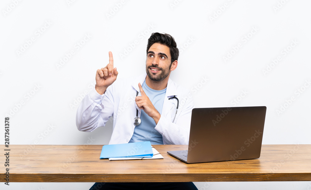 Young doctor man with his laptop over isolated wall pointing with the index finger a great idea Young doctor man with his laptop over isolated wall pointing with the index finger a great idea