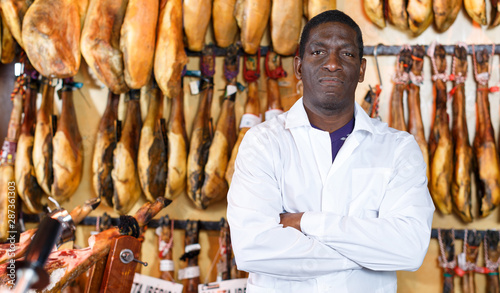 Confident shop owner near counter with ham