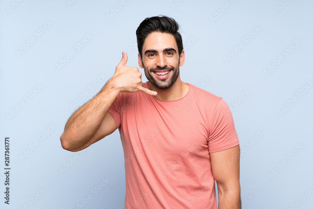Fototapeta premium Handsome young man in pink shirt over isolated blue background making phone gesture. Call me back sign