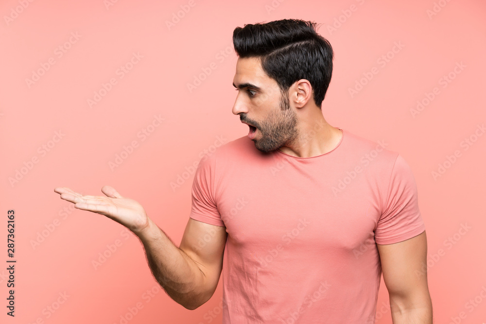 Handsome young man over isolated pink background holding copyspace imaginary on the palm