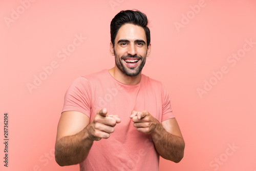 Handsome young man over isolated pink background points finger at you