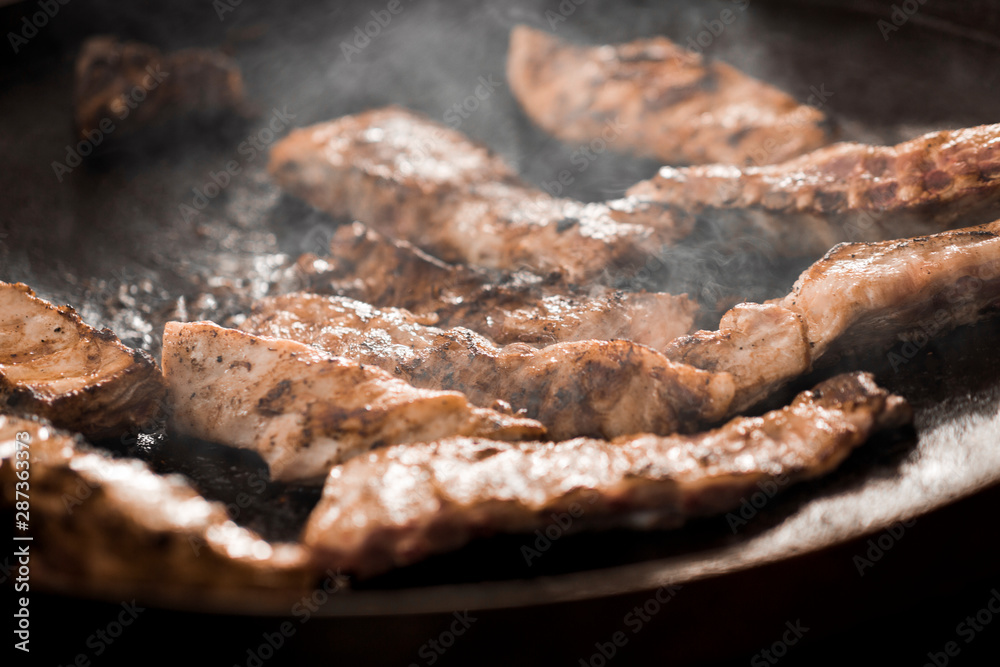 Close up of grilled meat on grid on black background with steam Close up of grilled meat on grid on black background with steam