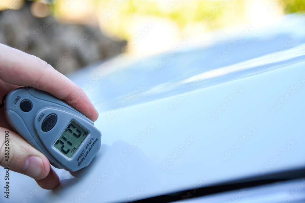 Male hand holds device for measuring coating thickness before polishing car. Measuring thickness of the car paint coating with paint thickness gauge. Polish car concept Male hand holds device for measuring coating thickness before polishing car. Measuring thickness of the car paint coating with paint thickness gauge. Polish car concept