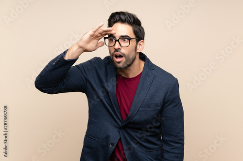 Handsome young man over isolated background looking far away with hand to look something