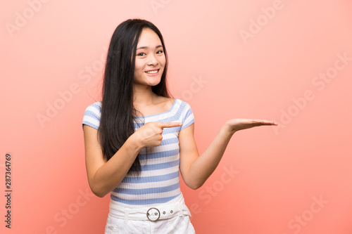 Teenager asian girl over isolated pink background holding copyspace imaginary on the palm to insert an ad © luismolinero