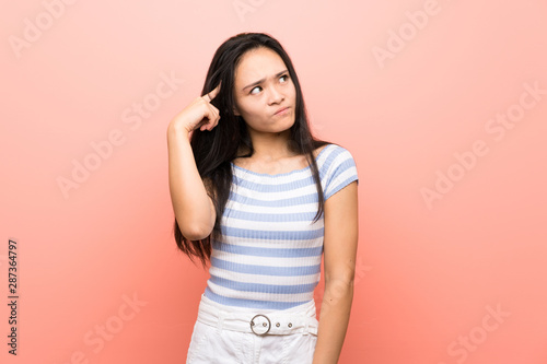 Teenager asian girl over isolated pink background making the gesture of madness putting finger on the head