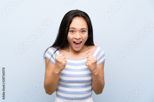 Teenager asian girl over isolated blue background celebrating a victory