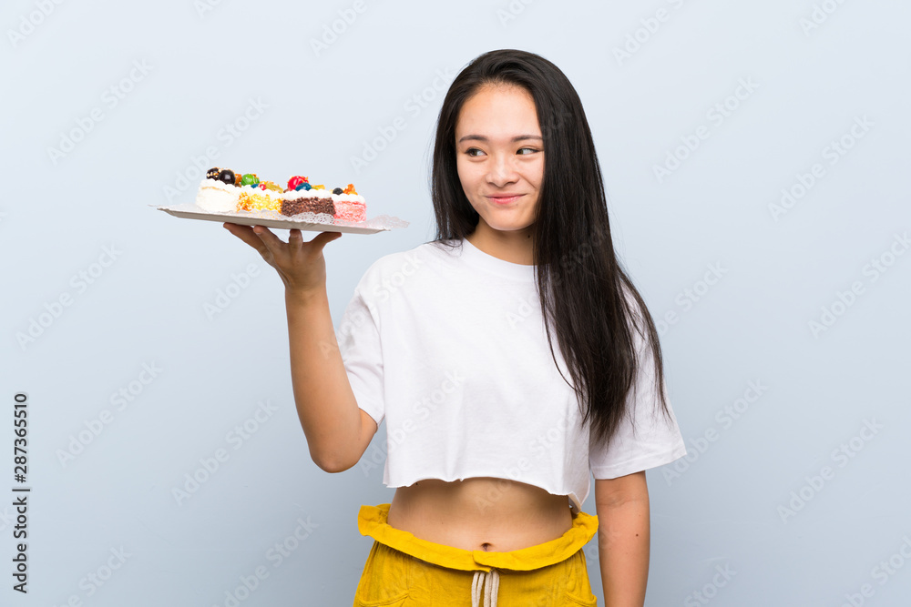 Teenager asian girl holding lots of different mini cakes with happy expression Teenager asian girl holding lots of different mini cakes with happy expression