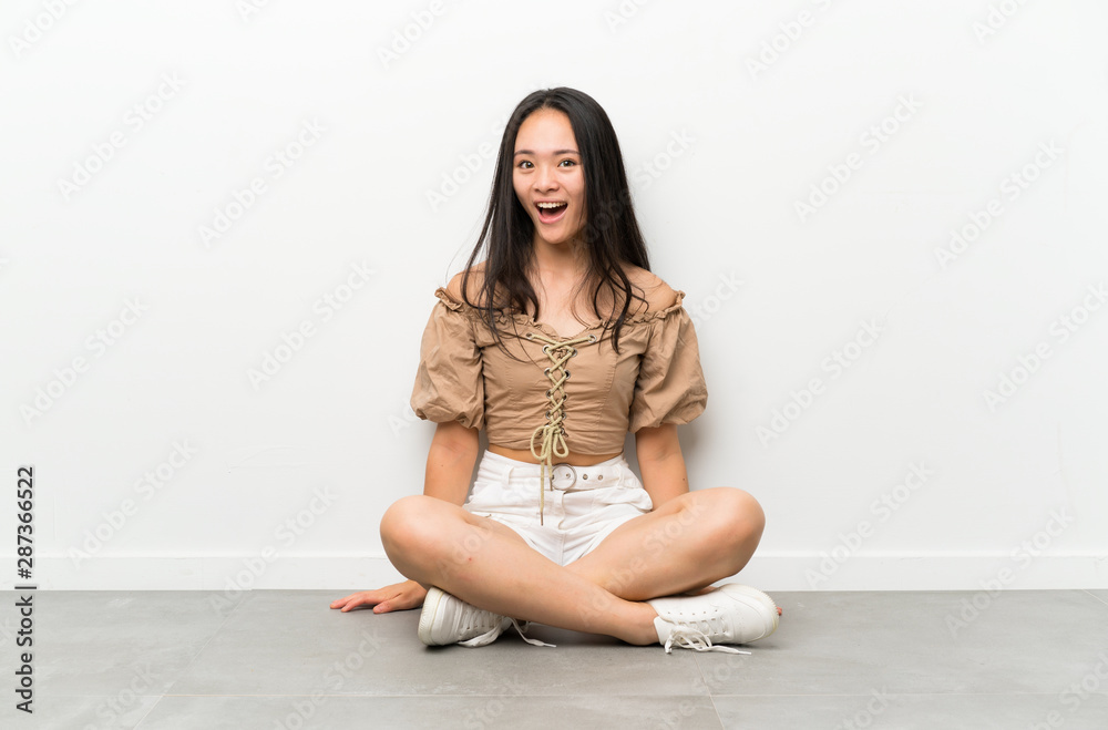 Teenager asian girl sitting on the floor with surprise facial expression Teenager asian girl sitting on the floor with surprise facial expression