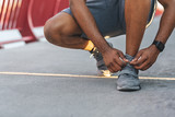 African american jogger checking on his shoelaces on bridge