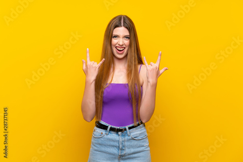 Young woman over isolated yellow background making rock gesture