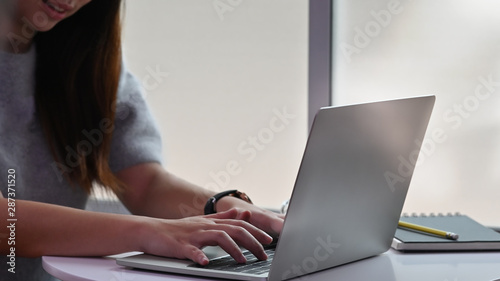 Close-up female typing laptop computer on table.