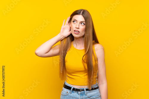 Young woman over isolated yellow background listening something