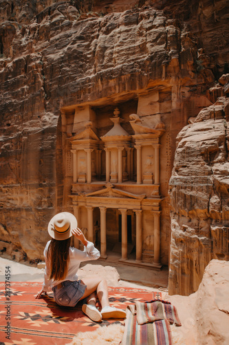 Young woman tourist sitting on a cliff after reaching the top, Al Khazneh in the ancient city of Petra, Jordan, UNESCO World Heritage Site