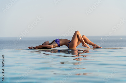 Young sexy woman in swimsuit reclining at the edge of infinity pool
