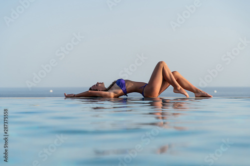 Young sexy woman in swimsuit reclining at the edge of infinity pool