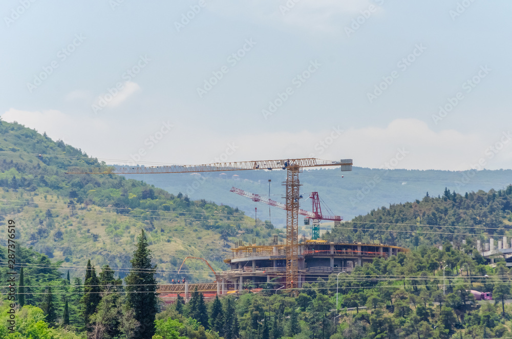 Construction site with cranes in the mountains. Construction activities in the mountains in Tbilisi Construction site with cranes in the mountains. Construction activities in the mountains in Tbilisi