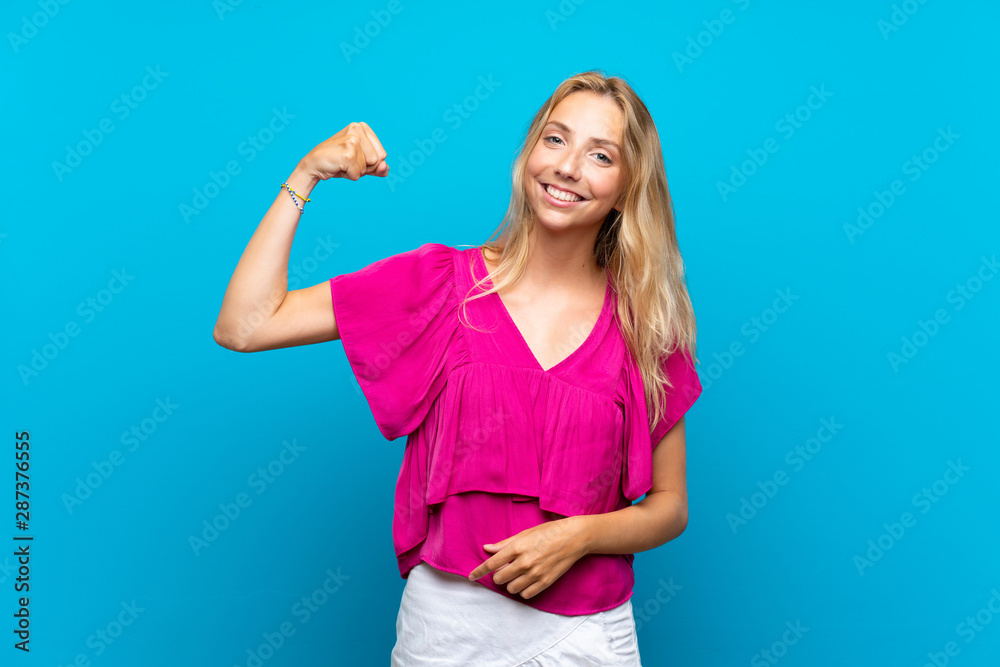 Fototapeta premium Blonde young woman over isolated blue background doing strong gesture