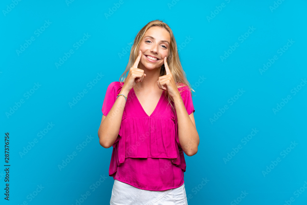 Blonde young woman over isolated blue background smiling with a happy and pleasant expression Blonde young woman over isolated blue background smiling with a happy and pleasant expression