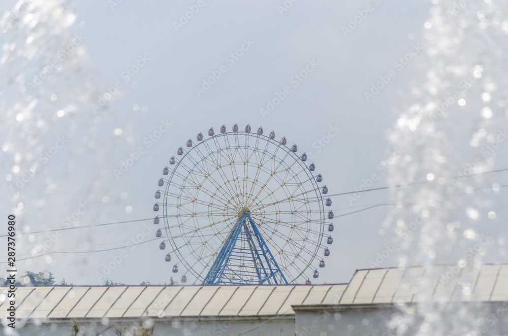 Ferris wheel with colored cabins in the amusement Park with a stream from the fountain on the sides in Sunny weather, Tbilisi