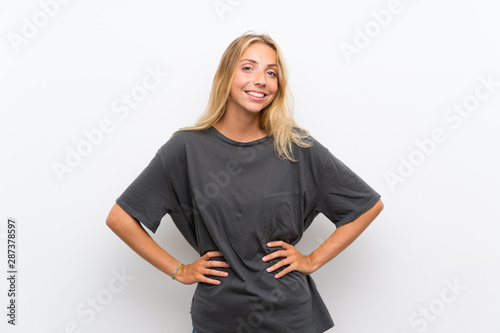 Blonde young woman over isolated white background posing with arms at hip and smiling