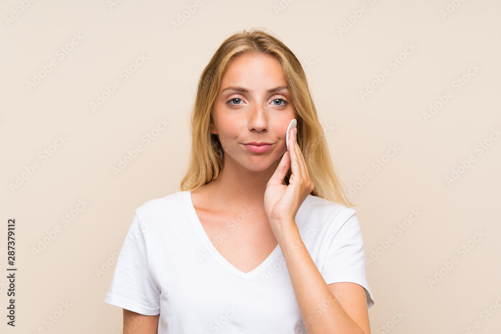 Young blonde woman removing makeup from her face with cotton pad Young blonde woman removing makeup from her face with cotton pad