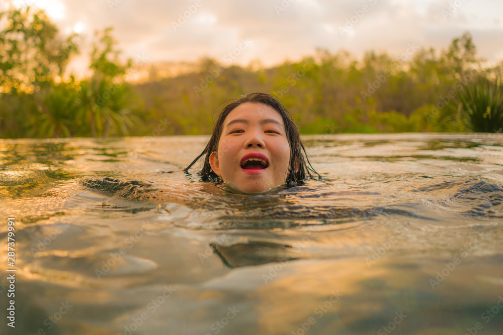 Fototapeta premium tropical holidays lifestyle portrait of young beautiful and happy Asian Korean woman in bikini enjoying sunset at amazing jungle resort infinity pool swimming relaxed