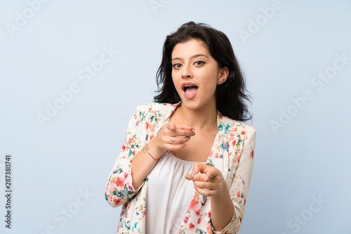 Young woman over isolated blue background points finger at you
