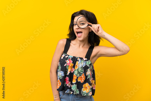 Young woman over isolated yellow background holding a magnifying glass