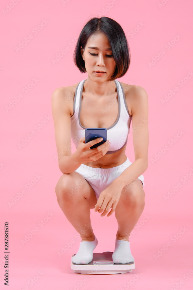 Healthy woman standing on weight scales feeling surprised in home on pink backgrounds, Healthy concept, Diet concept Healthy woman standing on weight scales feeling surprised in home on pink backgrounds, Healthy concept, Diet concept