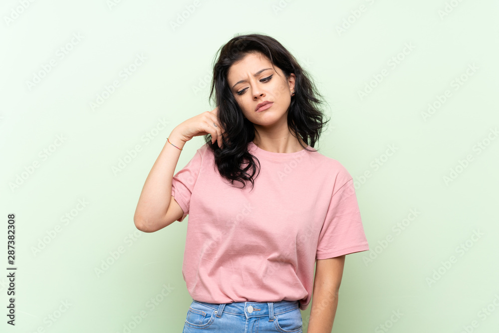 Young woman over isolated green background making the gesture of madness putting finger on the head Young woman over isolated green background making the gesture of madness putting finger on the head