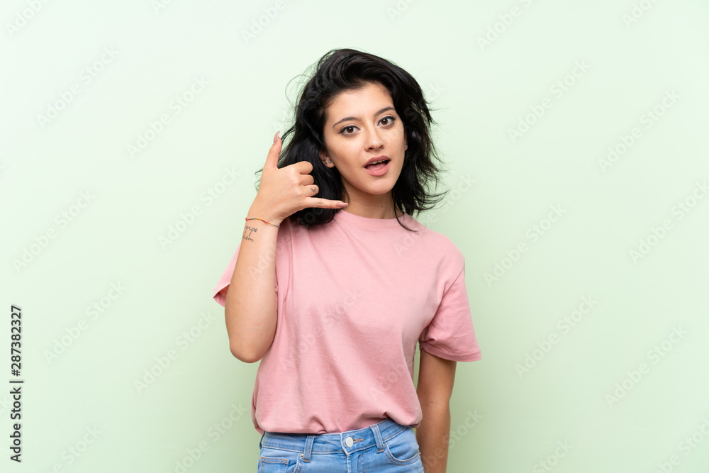 Young woman over isolated green background making phone gesture. Call me back sign Young woman over isolated green background making phone gesture. Call me back sign