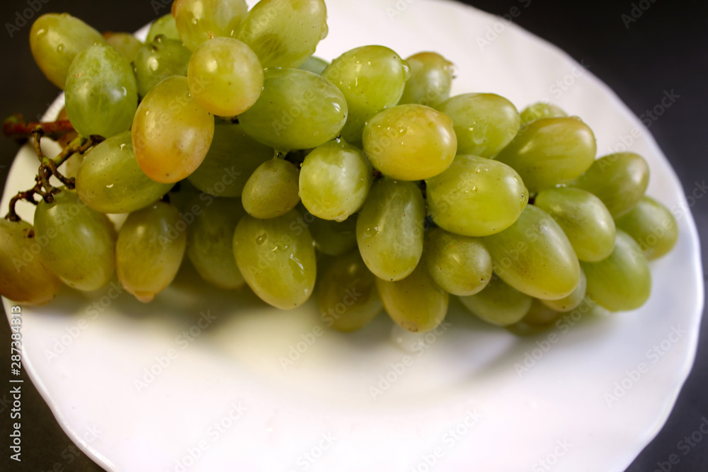 Bunch of green grape isolated on a plate on a black background Bunch of green grape isolated on a plate on a black background