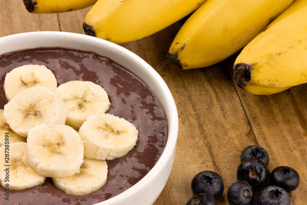 bowl of acai smoothie with banana slices on top and bunch of bananas in the background bowl of acai smoothie with banana slices on top and bunch of bananas in the background
