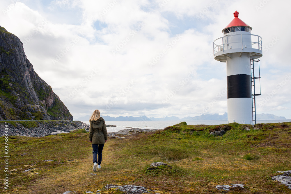Blond hair woman walks near the lighthouse and enjoy beautiful nature landscape. Lonely girl. Amazing scenic outdoors view in North. Travel and adventure. Explore Norway. Lofoten Islands. Scandinavia