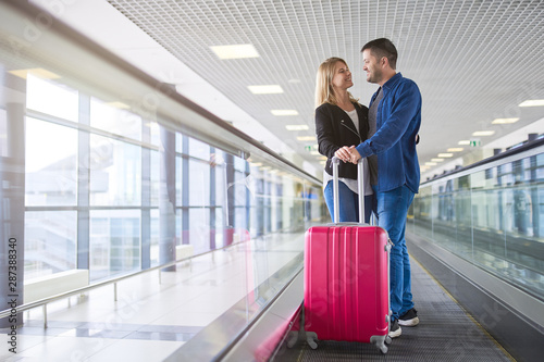 Photo from side of happy man and woman with suitcases in transit at airport