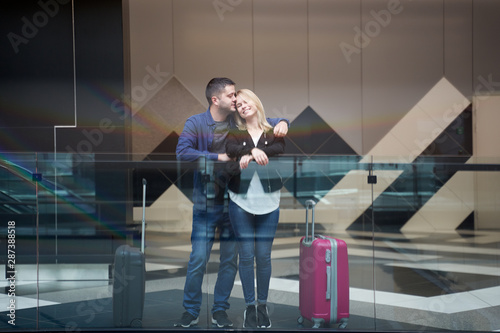 Photo of cuddling man and woman standing with suitcases at airport