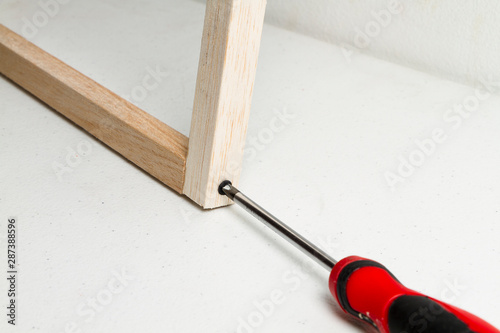 Destornillador rojo uniendo dos palos de madera de balso con tornillo negro sobre un fondo blanco