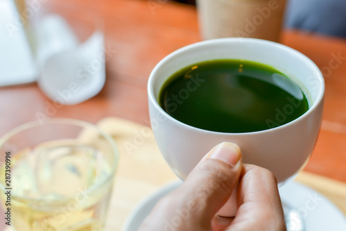 Hold hot matcha (green tea) in white ceramic cup on hand served on wooden tray on table in cafe and coffee shop. Healty beverages of japan for reduce sugar in blood.