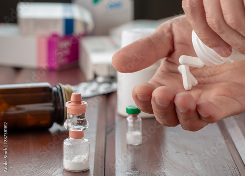 A man s hand holds a white pill and a bottle of pills. In the foreground are bottles of powders for medicinal solutions