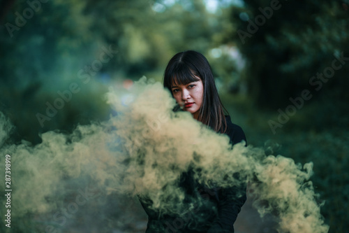 Portrait of Asian woman in black cloth with color fire smoke in forest witch concept © chayathon2000